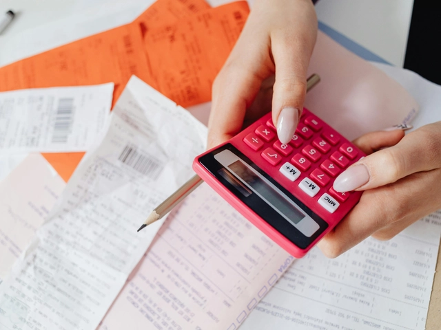 A woman's hands hold a red calculator over a pile of receipts and papers